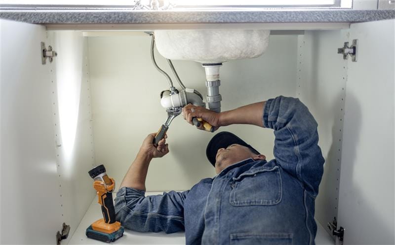 Plumber repairing pipes beneath a bathroom sink in Evans