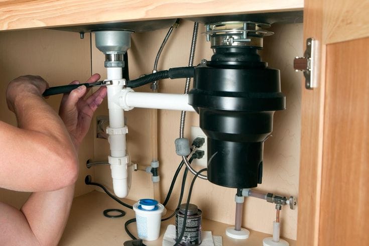 Plumber installing a garbage disposal beneath a kitchen sink in Evans