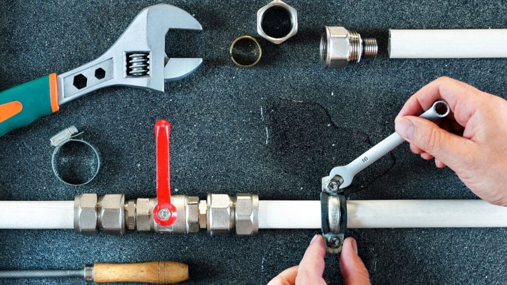Plumber repairing a pipe valve with an adjustable wrench in Evans