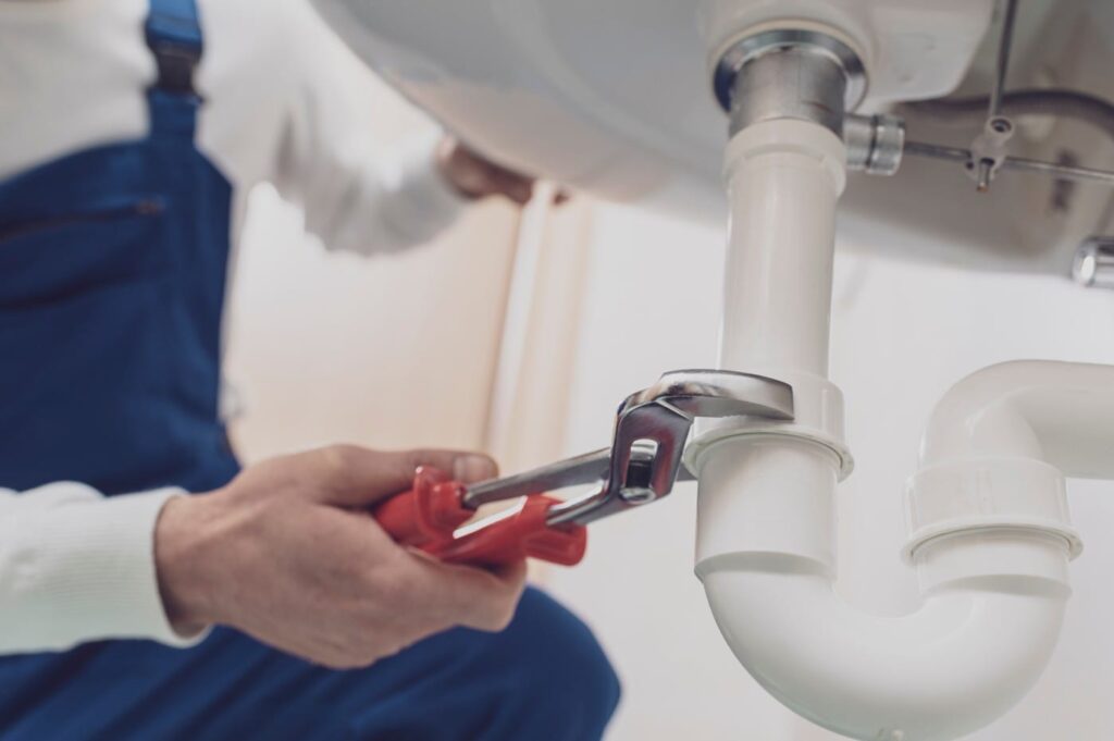 Plumber repairing a white drain pipe beneath a sink in Evans